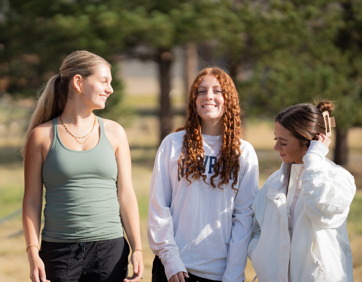 Three female students huddle for a photo together in a field.