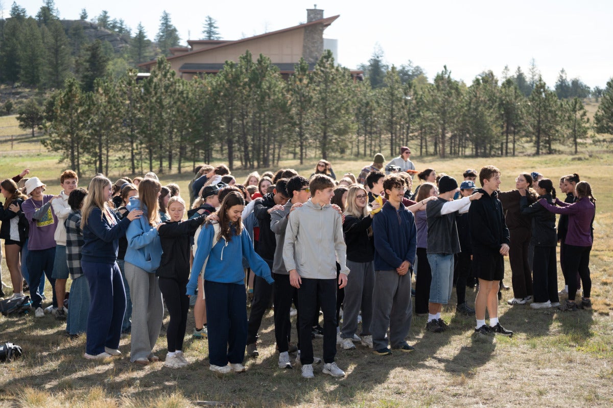 Students form lines and put their hands on each other's shoulders for an icebreaker game.