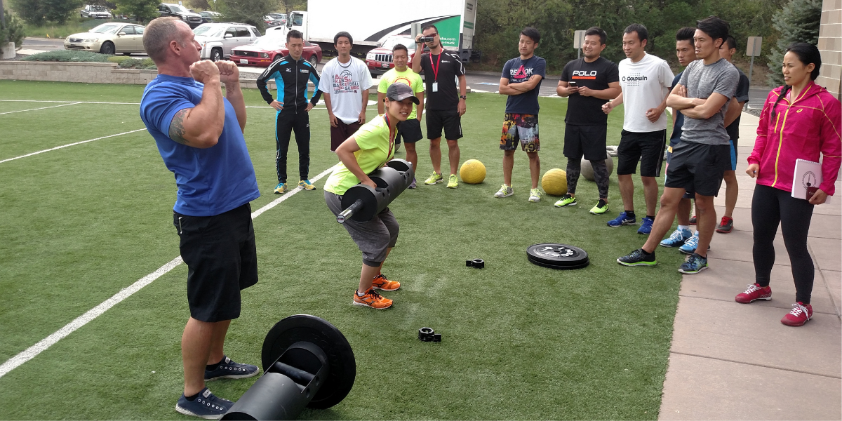 coach lifting weights with athletes on a field