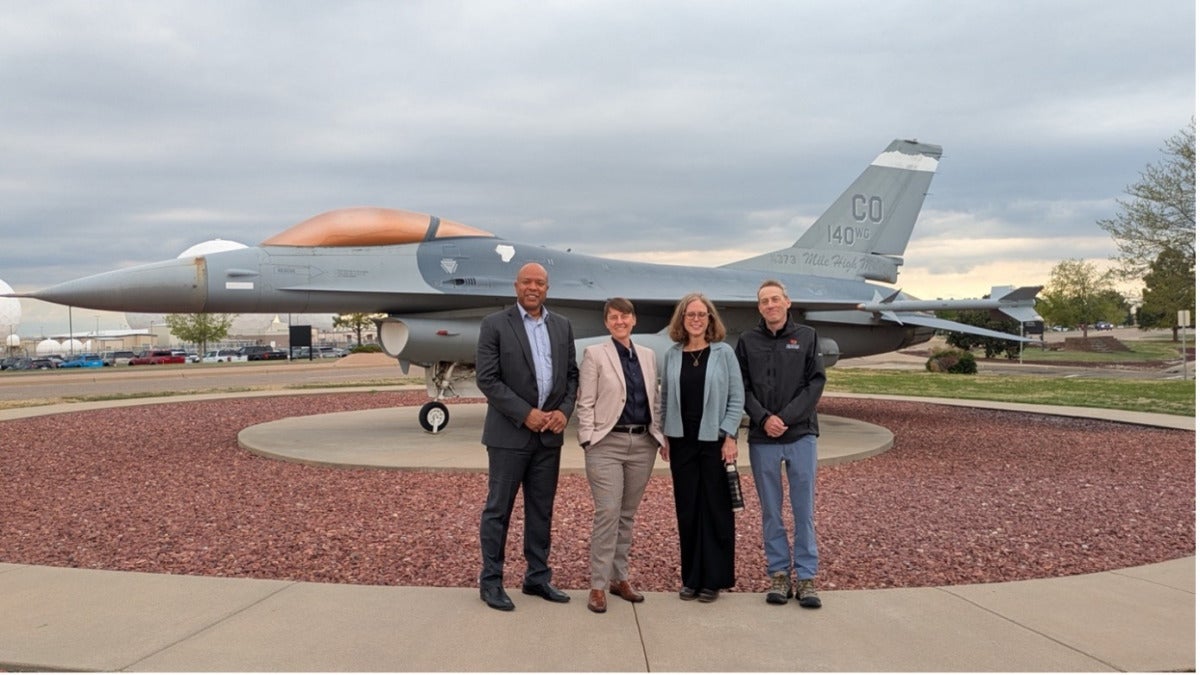 Four people stand in front of a jet.