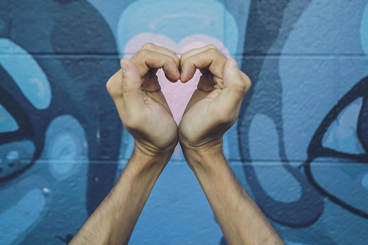 two hands making a heart in front of street mural