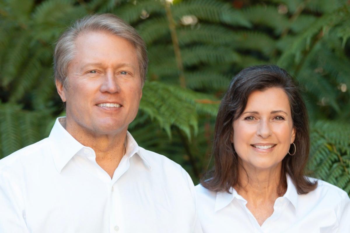 Denise O'Leary and her husband, Kent Thiry, pose for a photo together in front of large ferns.