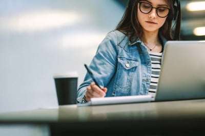 a student works at a laptop while writing on pad of paper