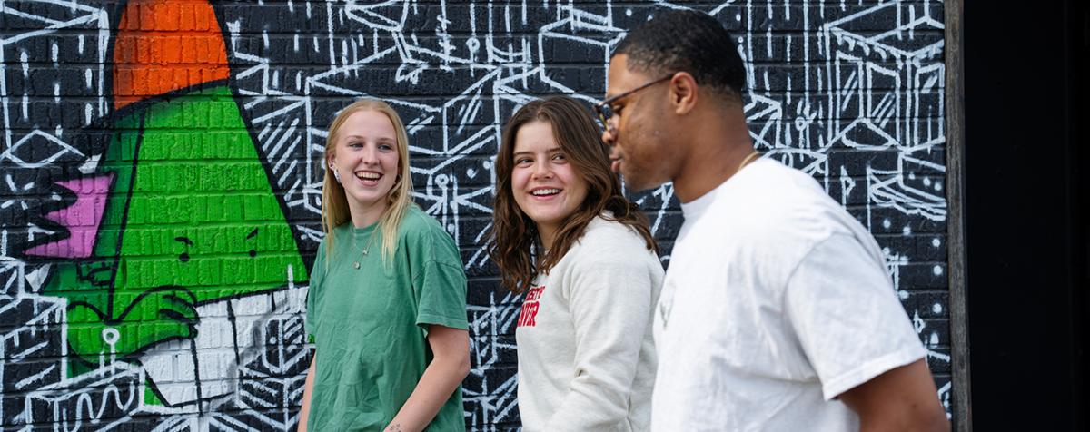 Three University of Denver students walking together near a colorful mural.