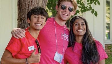 Three students in bright red t-shirts huddle for a group photo under a tree.