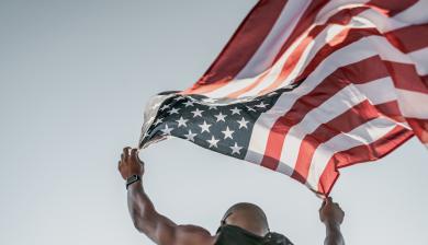 a man holding an american flag blowing in the wind