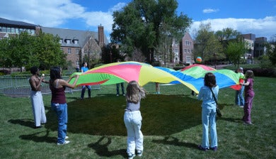 Students play with a rainbow parachute during DU's Day of Play on the Campus Green.