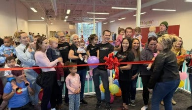Surrounded by supporters, Jessica Lopez cuts a big red ribbon on her new business, Little Legends Athletics.