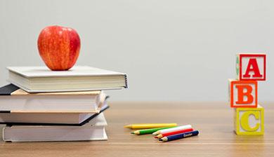apple on stack of books next to colored pencils and a b c blocks on desk