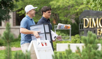 A lacrosse student at DU helps a man haul a bin on the sidewalk near the Dimond Family Residential Village.