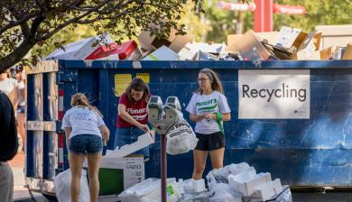 DU students throw items into a dumpster marked "recycling."
