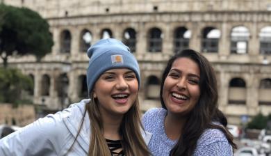 Two students smile together outside of the Coliseum in Rome.