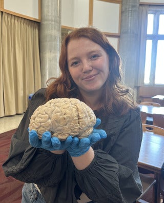 Student Olivia Marker holds a brain while wearing blue latex gloves in a campus lab.