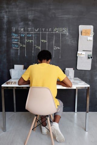 student working at desk with chalkboard calendar in front of him