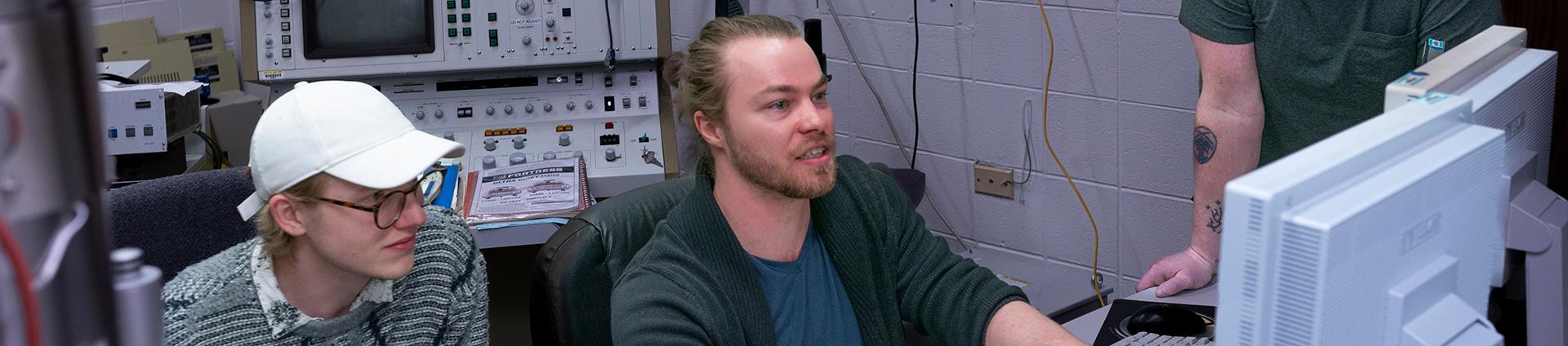 three researchers looking at computers in physics lab