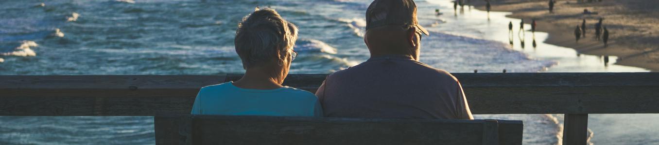 A couple sits at a pier overlooking the beach