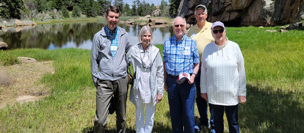 group of five older men and women standing in front of mountain lake
