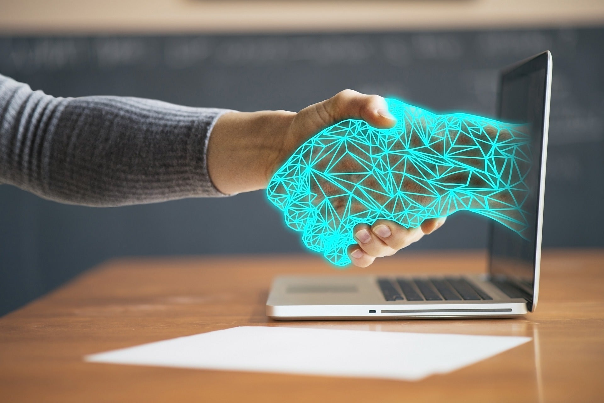 human hand shaking a digital hand through a computer