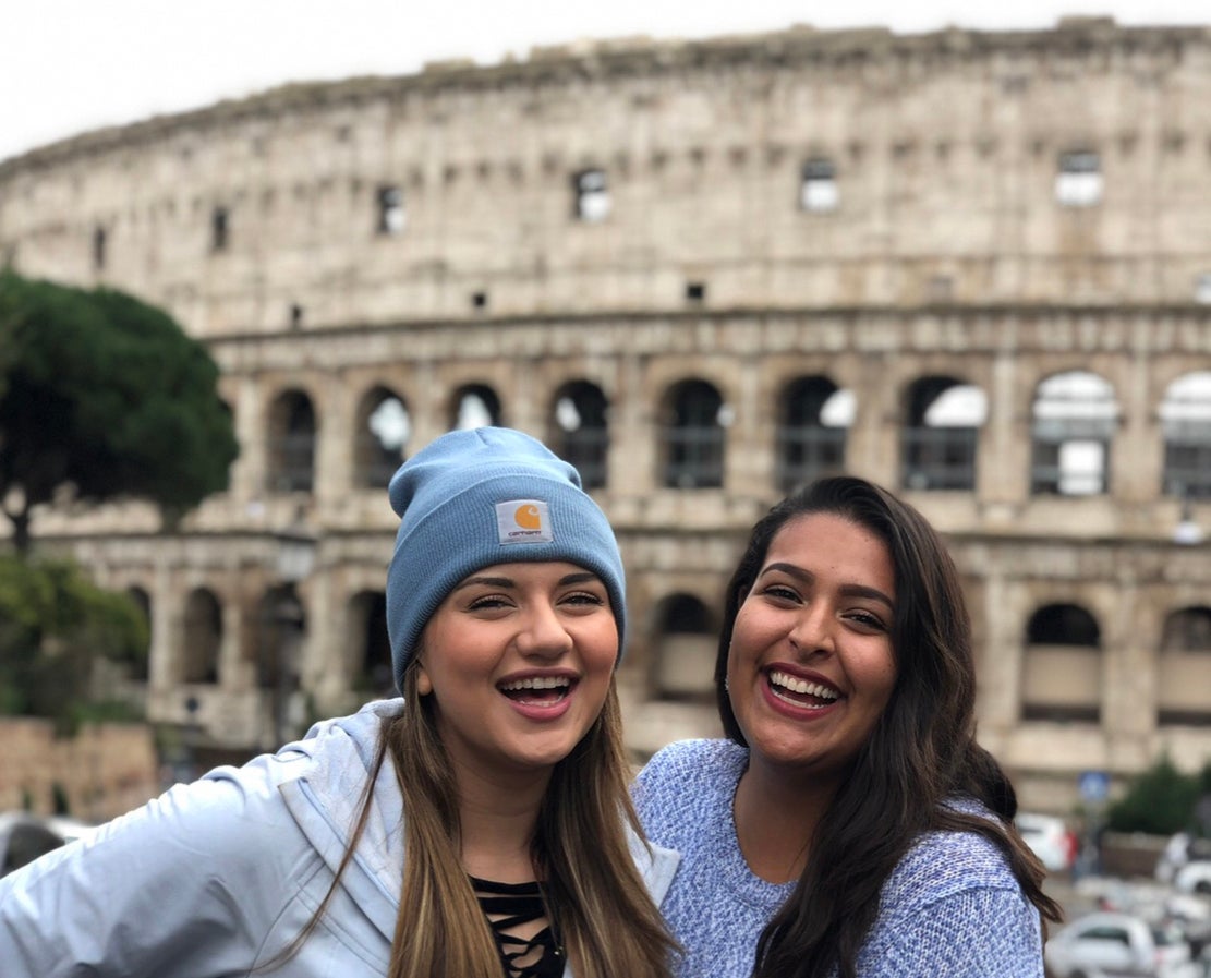 Two students smile together outside of the Coliseum in Rome.