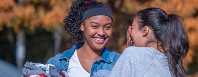 women laugh while talking outside on campus